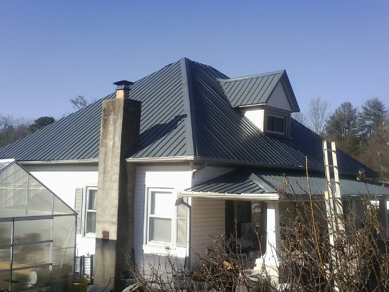 Dark blue standing seam metal roof on a white farmhouse with dormer — Slate & Tile Roof Repair by Roofing Brothers in Greenvale