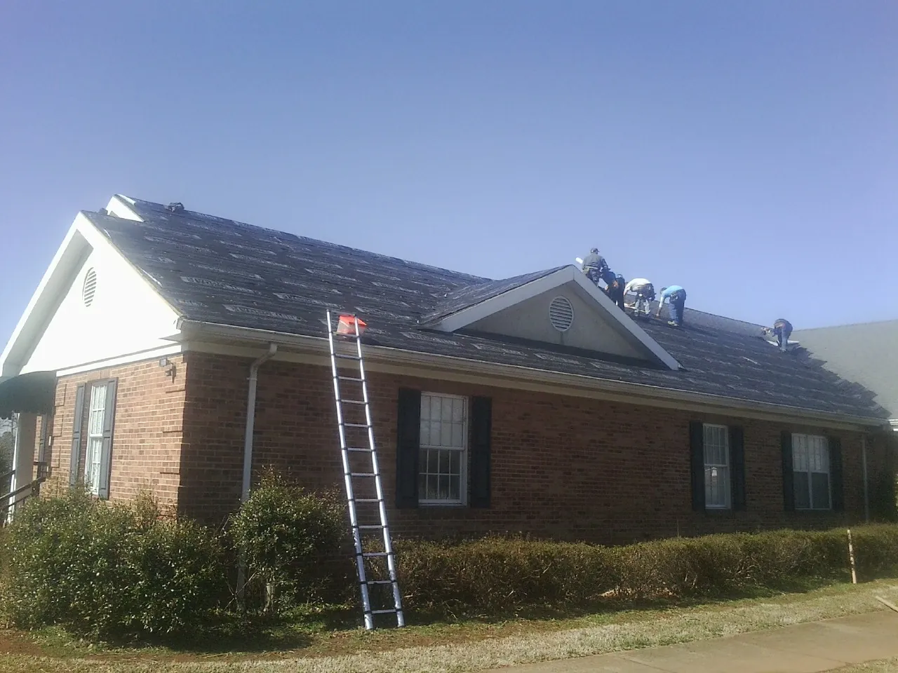 Crew tearing shingles off a brick ranch roof with a ladder set — Metal Roof Repair work by our crew in Greenvale