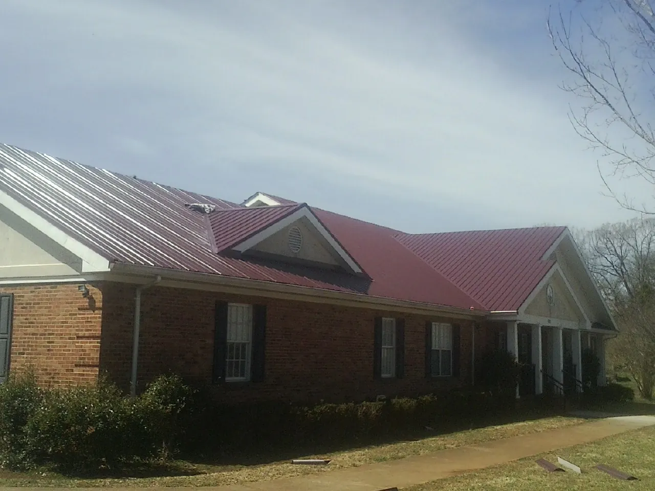 Red metal roof with gabled entries on a long brick building, from a Hail Damage Roof Repair job in Greenvale