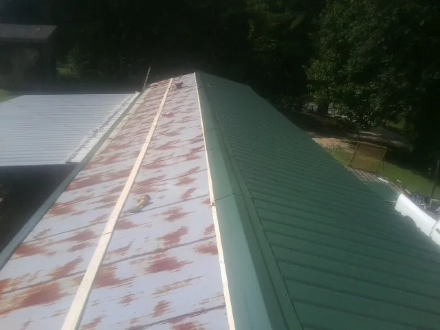 Old rusted panels beside newly installed green metal roofing — Wind Damage Roof Repair by Roofing Brothers in Greenvale