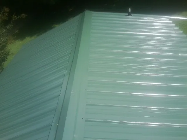 New green metal panels meeting at the ridge of a roof — Flat Roof Repair work by our crew in Greenvale