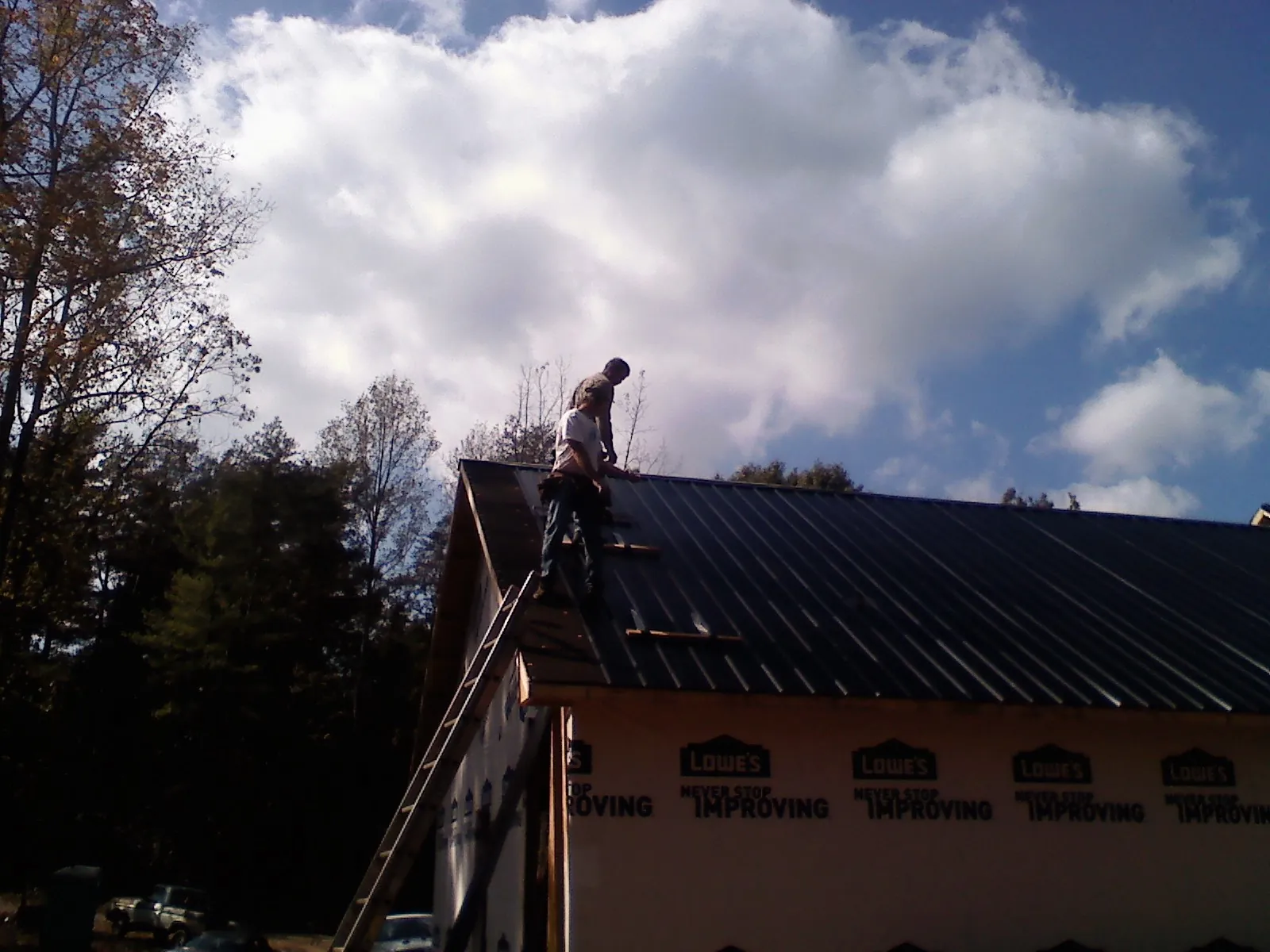 Roofer fastening dark metal panels high against a cloudy sky, from a Roof Inspection job in Greenvale