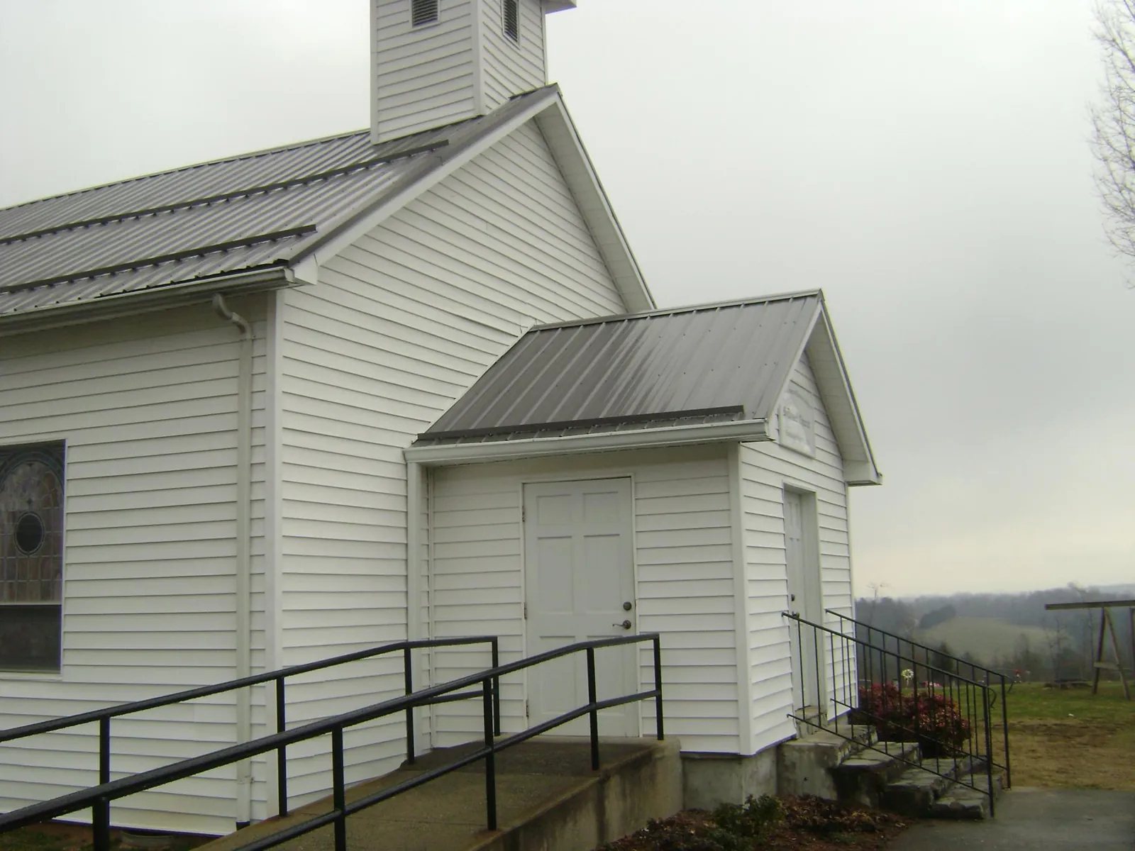 Gray metal roof on a white clapboard church with a steeple in Greenvale