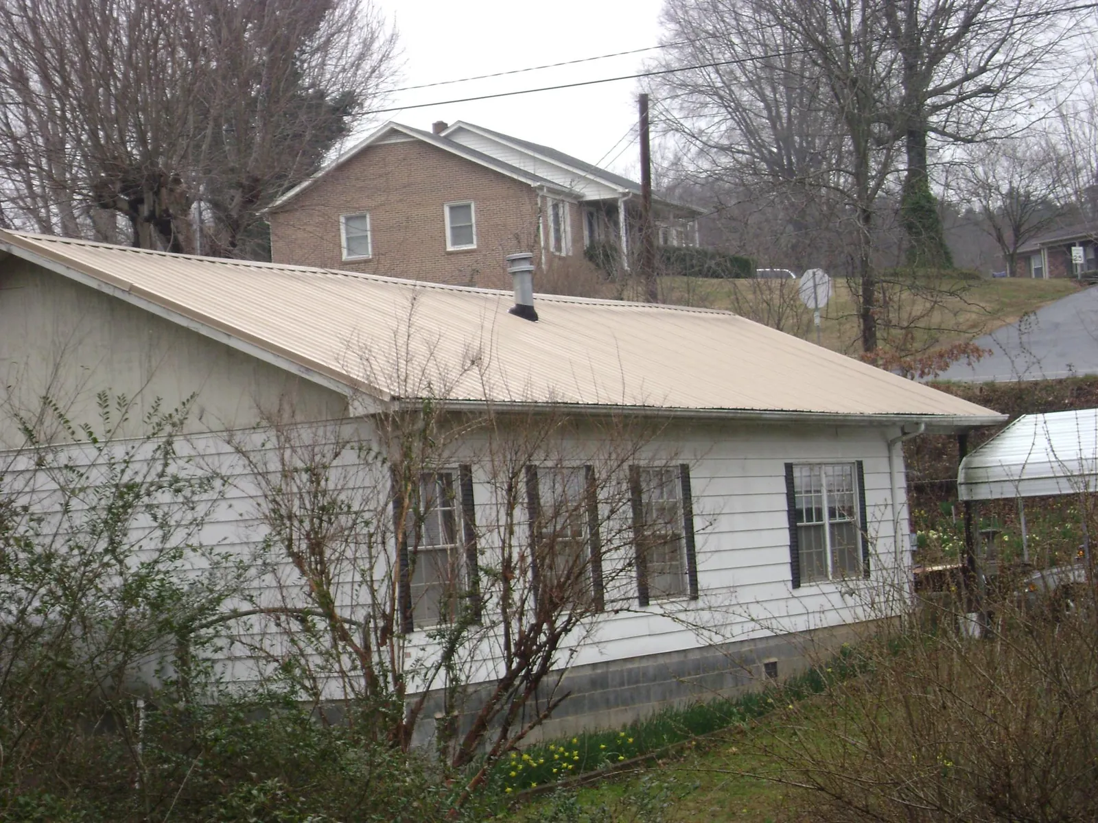 Tan metal roof on a white sided house set into a hillside — Commercial Roofing by Roofing Brothers in Greenvale