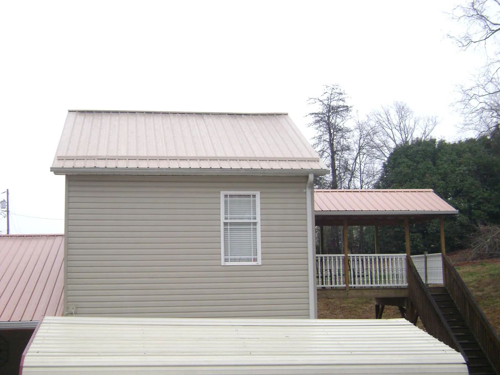 Tan metal roofs on a two story addition and attached porch, from a Roof Replacement job in Greenvale